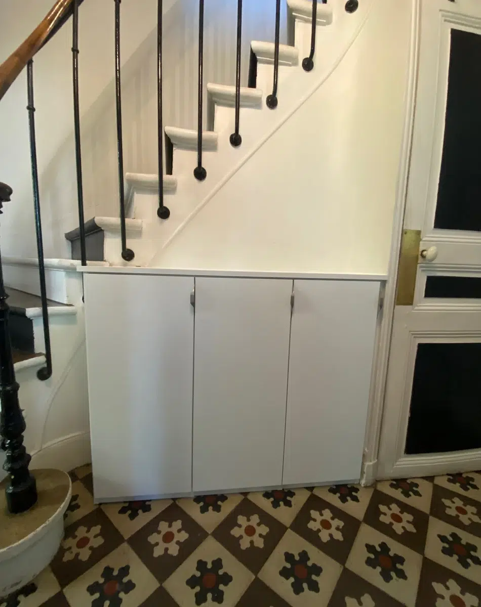 Placard blanc sous escalier avec carrelage géométrique.